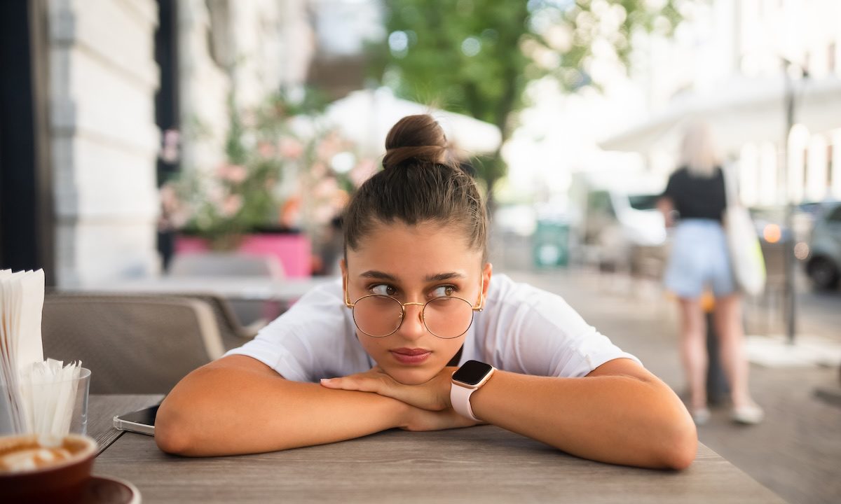 Bored, indifferent girl at a table in a street cafe with a Cup of coffee