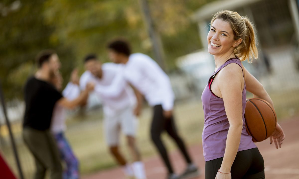 Portrait of fitness young woman with basketball ball playing game outdoor with friends