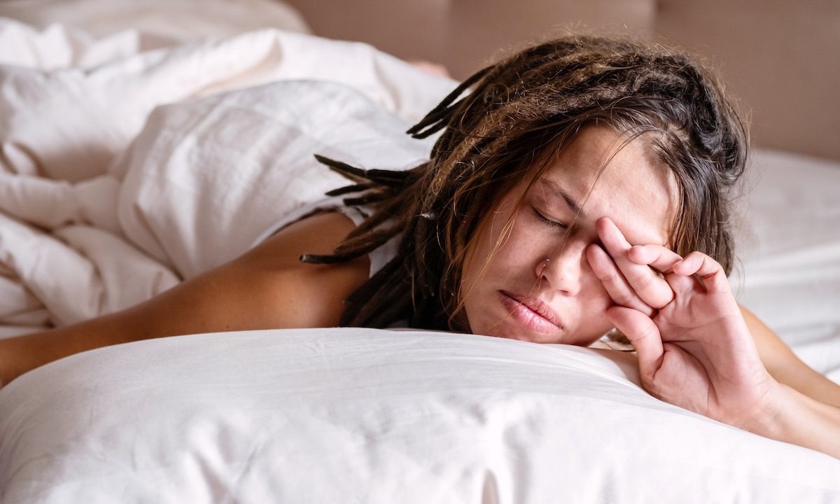 Woman covering his eyes from the morning light in the bed.