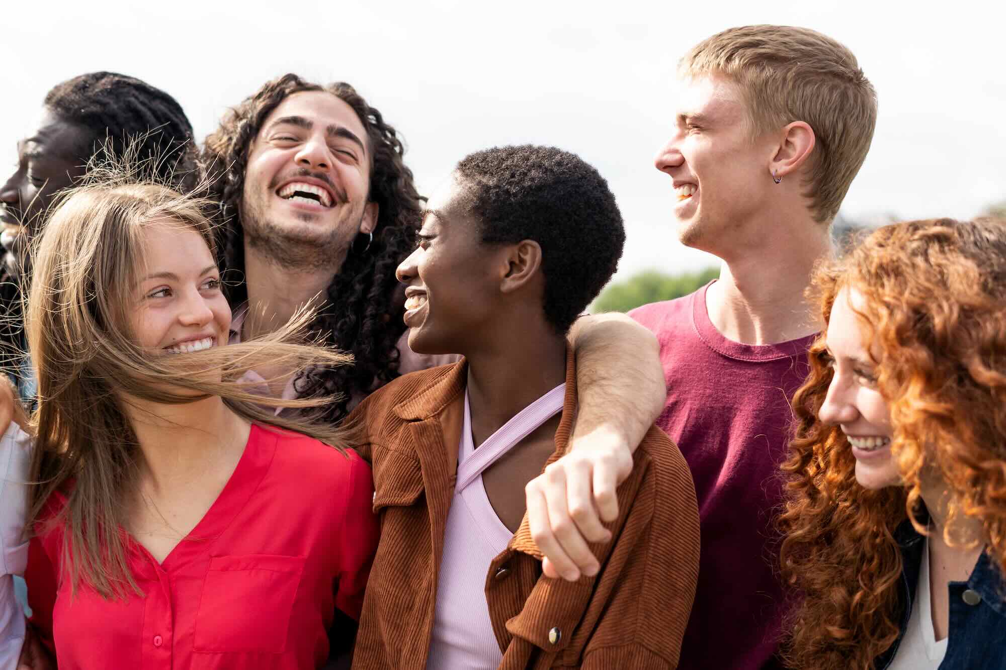 Multiracial group of friends embrace and enjoy a beautiful day together in the city park. They are laughing and smiling while they spend time together in nature