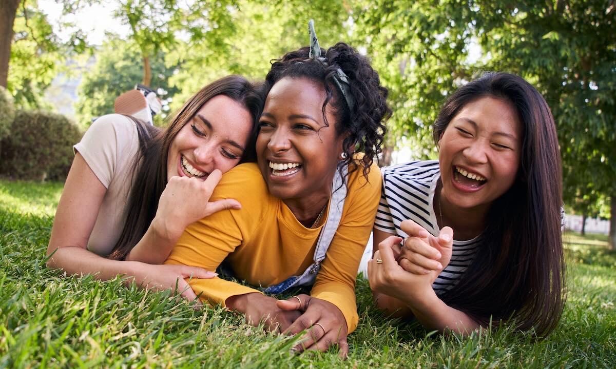 Three Women Smiling And Relaxing On The Grass In A Park