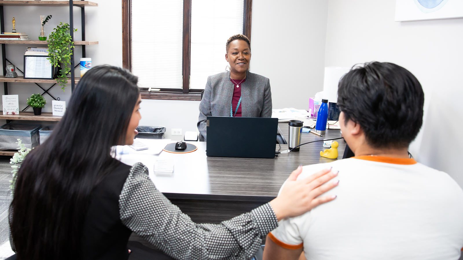 A counselor and two clients having a discussion across a desk.