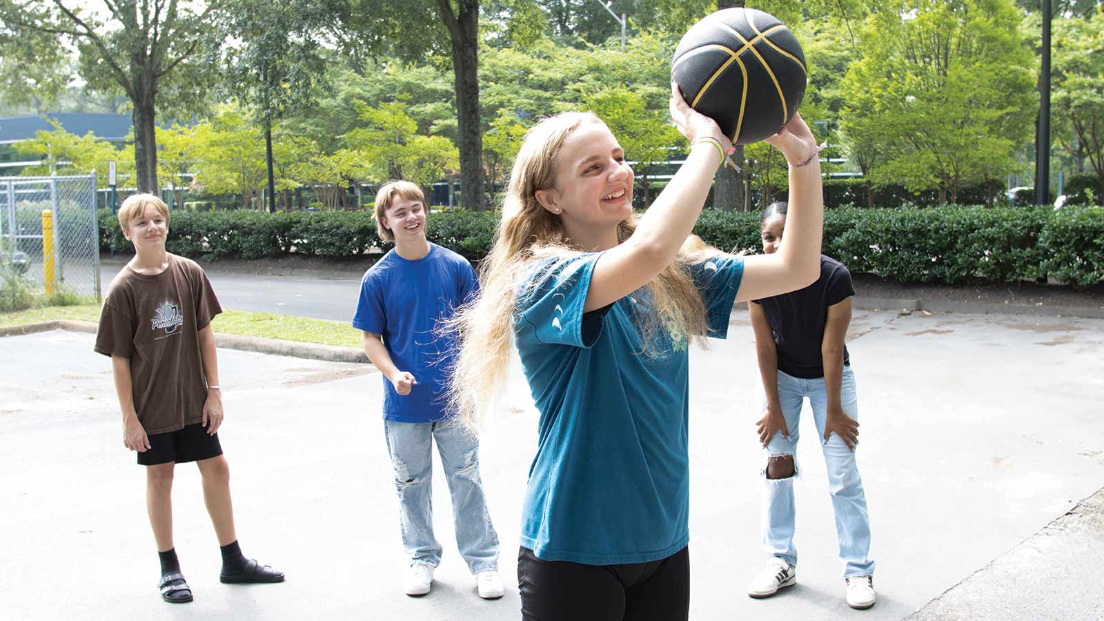 four teens outside playing basketball