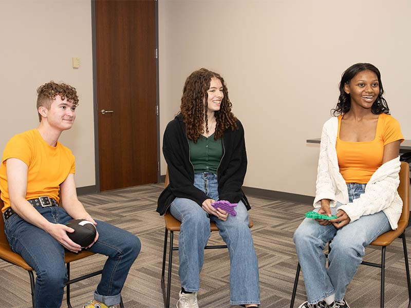 three girls and two boys sitting in chairs in a room