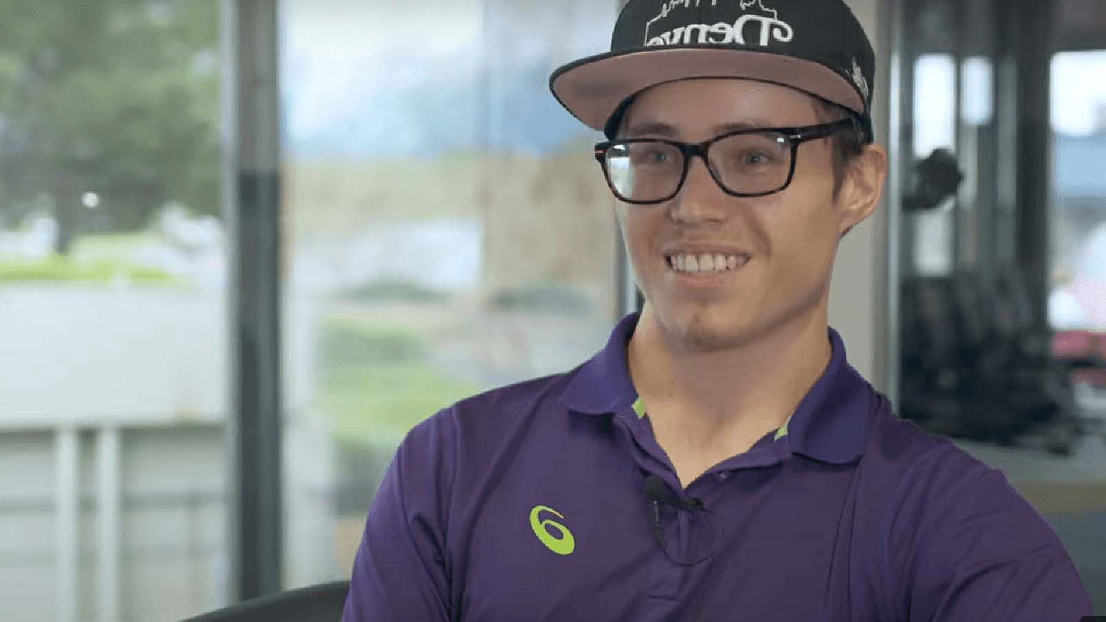 A smiling young man wearing glasses and a baseball cap