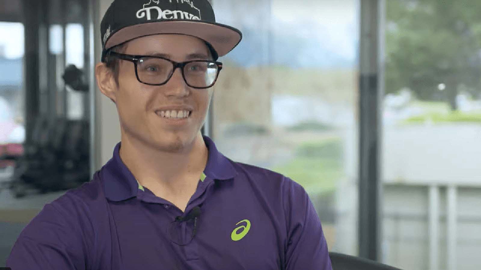 A smiling young man wearing glasses and a baseball cap