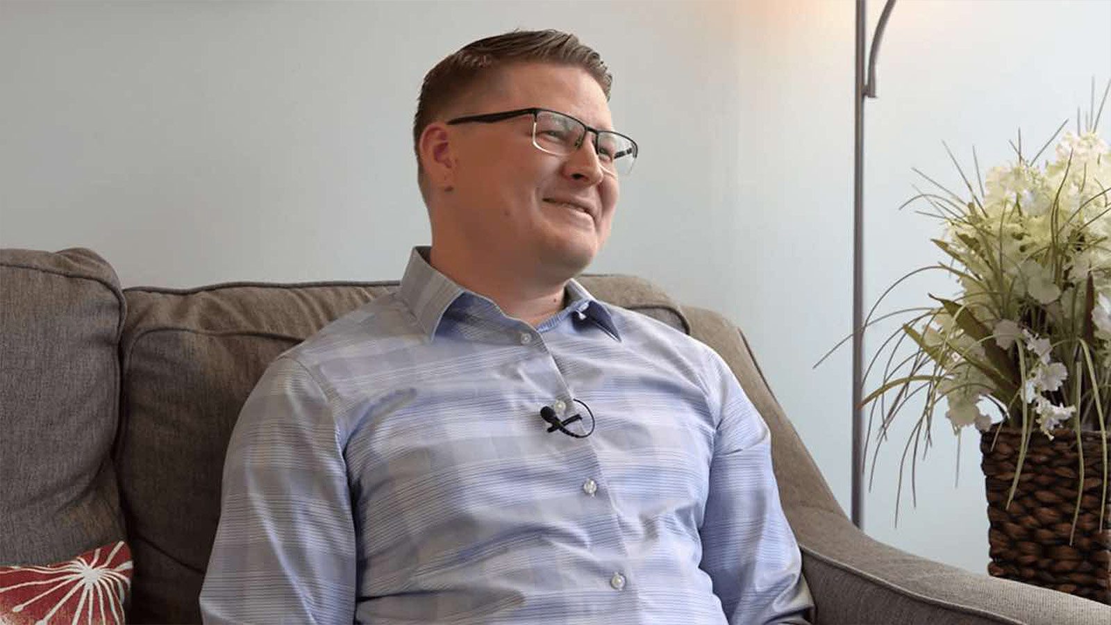 A man smiling, sitting comfortably on a couch in a cozy, well-decorated room.