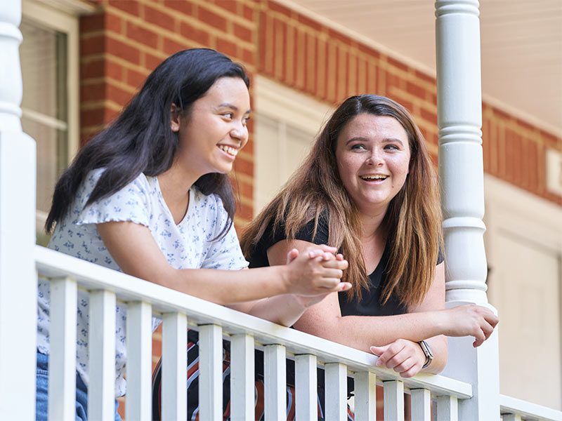 two women standing on a porch with a brick building in the background