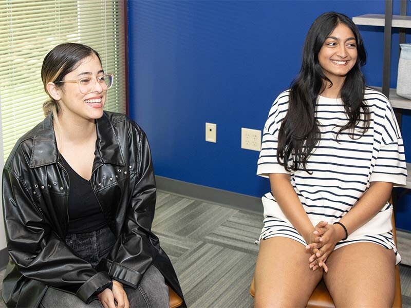 two women sitting on a chair in a room with a blue wall