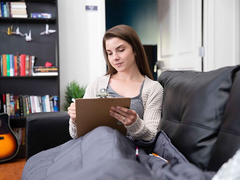 woman sitting on a couch reading a book while holding a clipboard