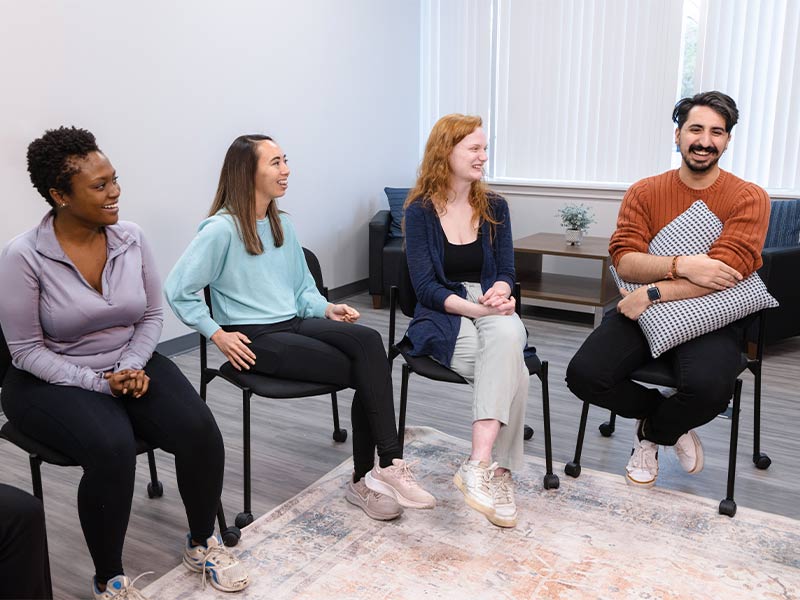 several people sitting in a circle in a room with a rug