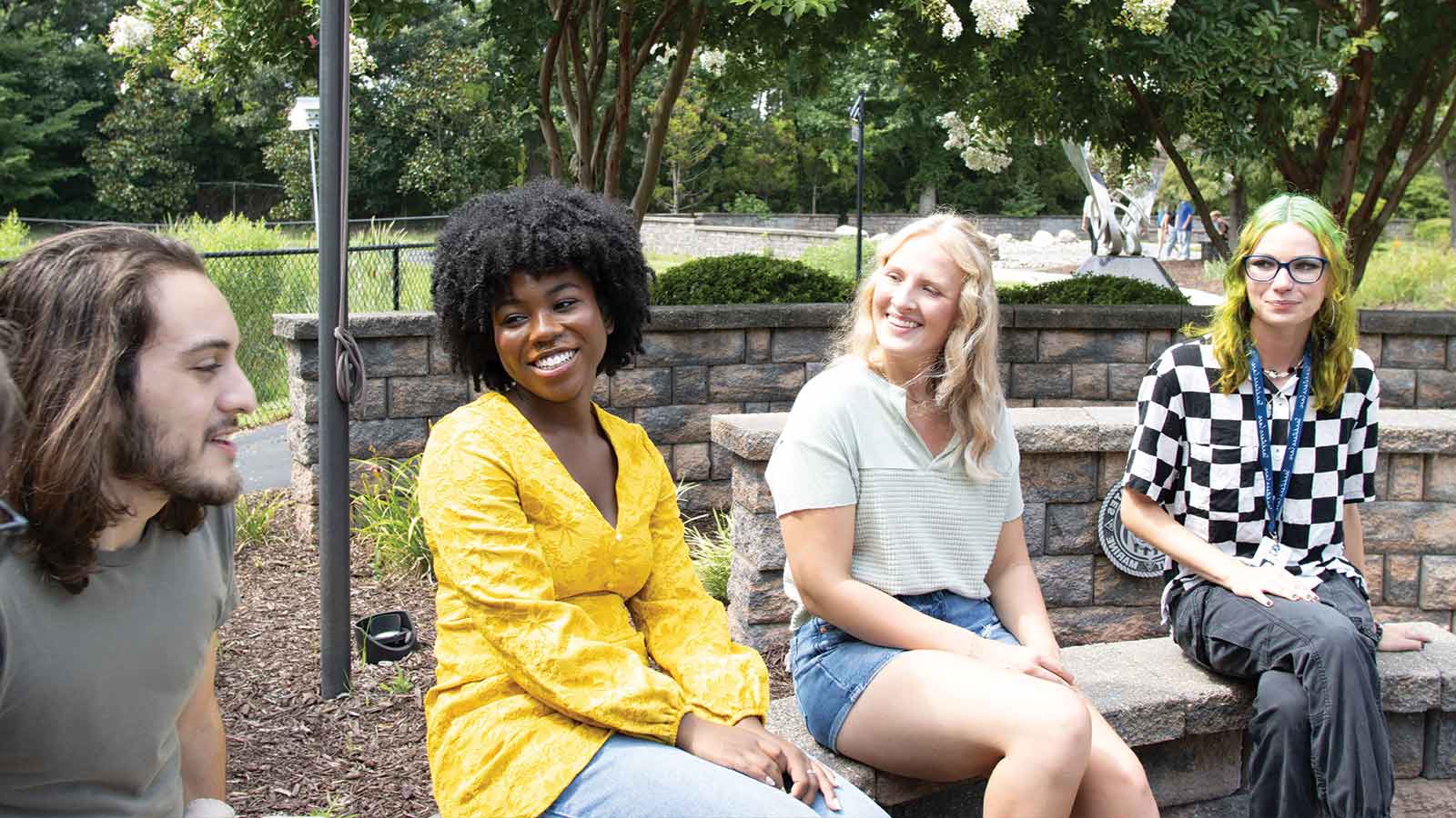 four young adults sitting outside on a bench