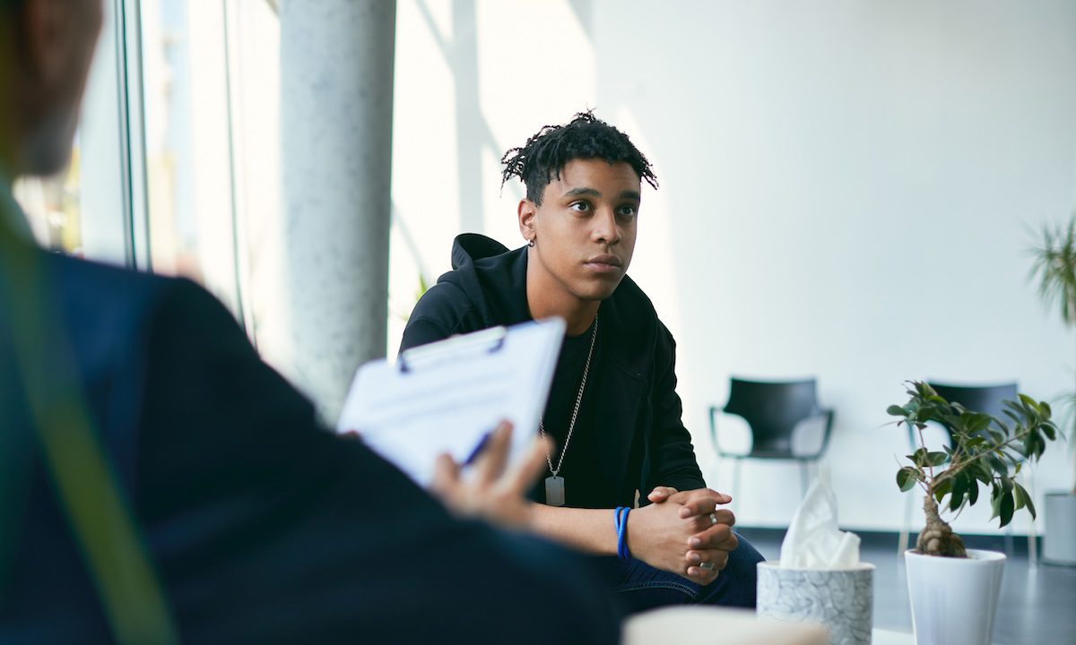 Black teenage boy having counselling with mental health professional during therapy session.