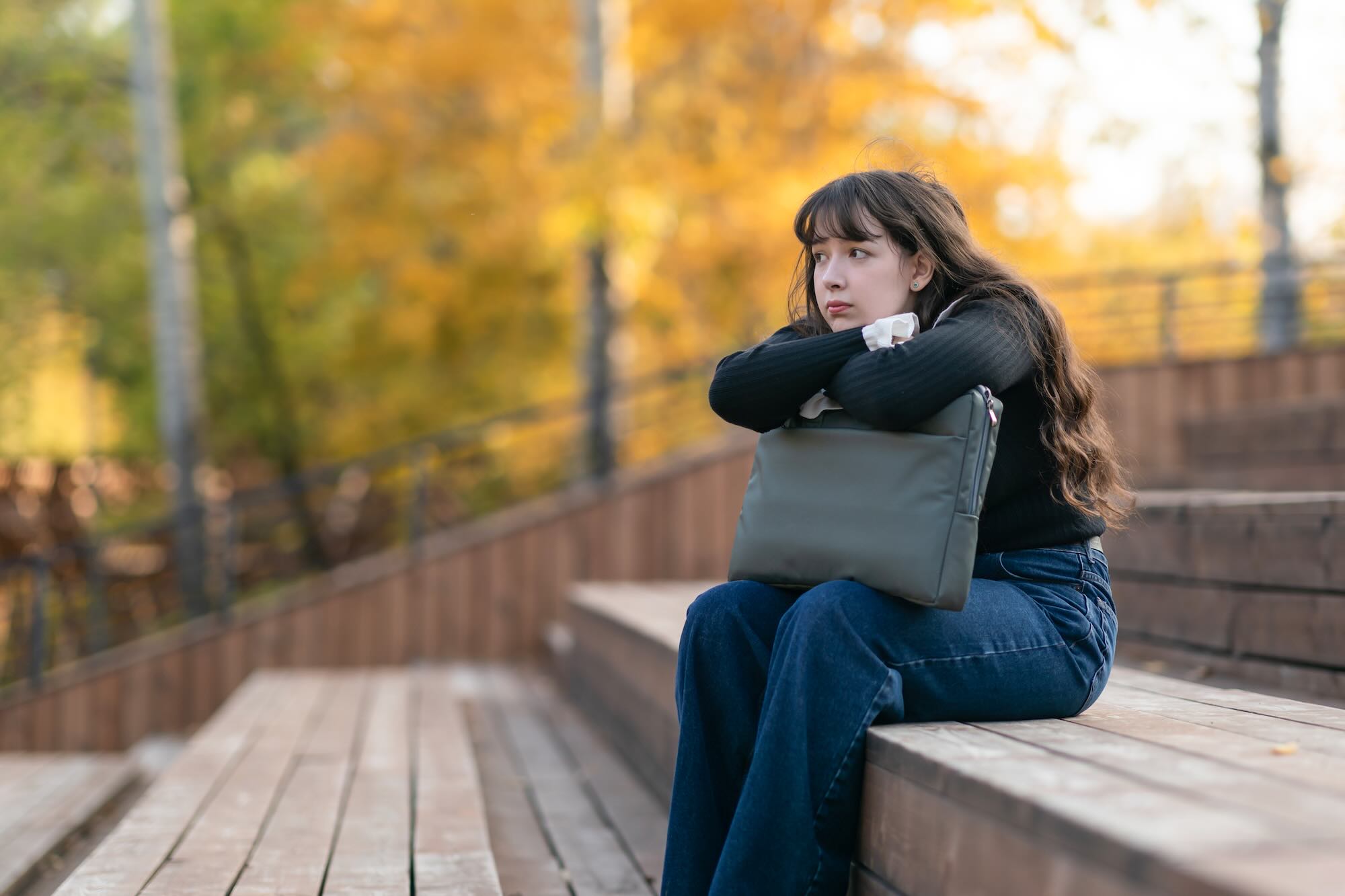 Side view young woman wearing stylish casual clothes use work on laptop sit on bench, relax in autumn city park outdoors on nature. Urban lifestyle concept