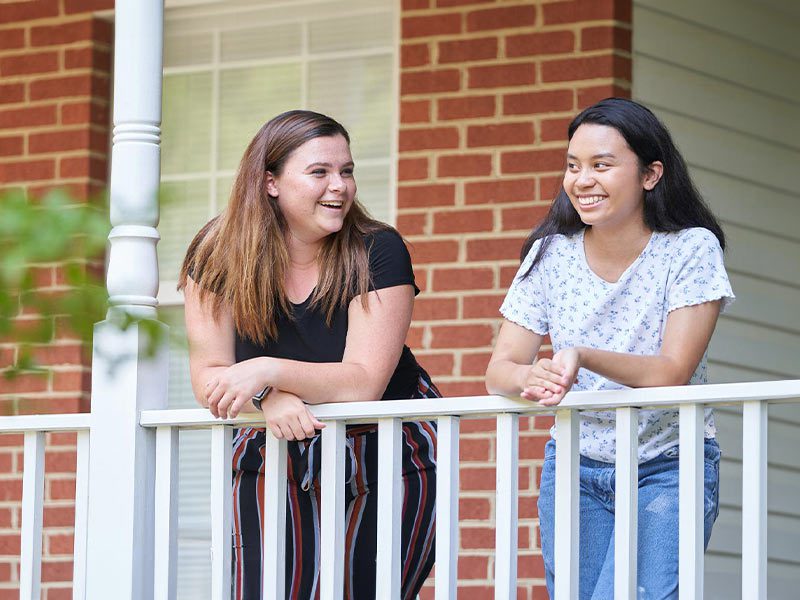 two teens girls outside talking on a porch